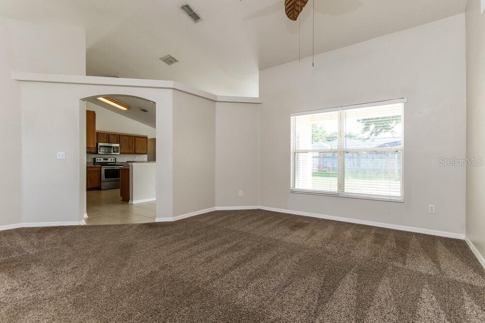 A carpeted living room with vaulted ceilings and a view into a kitchen — 9615 SARAGOSSA STREET, CLERMONT, FL