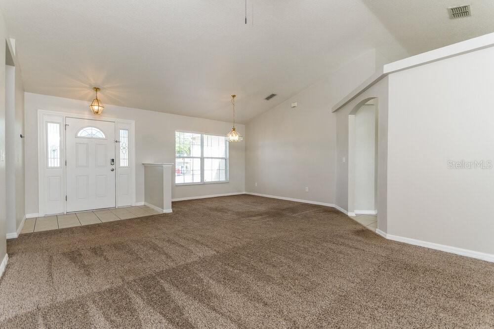A carpeted living room features a vaulted ceiling, a front door, and a dining area — 9615 SARAGOSSA STREET, CLERMONT, FL