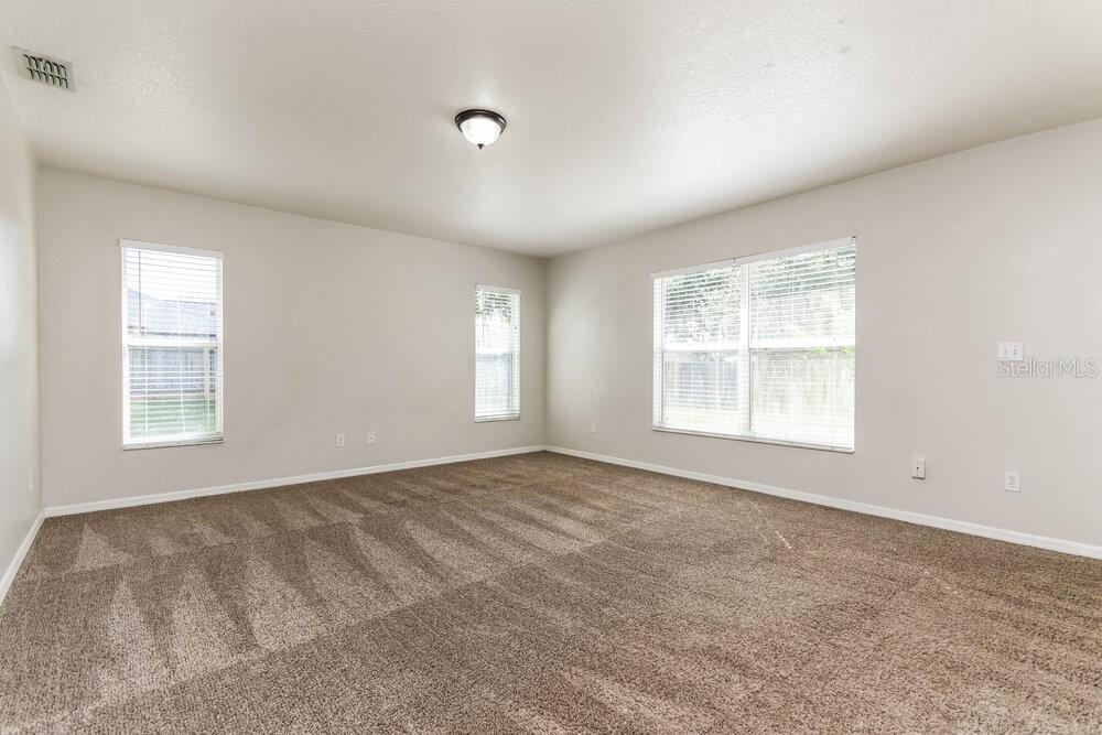 An empty room with beige walls, brown carpet, and two windows — 9615 SARAGOSSA STREET, CLERMONT, FL