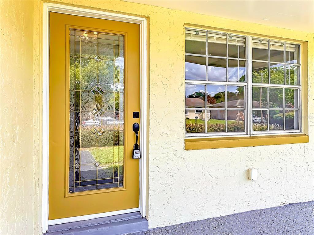 A yellow front door with a decorative glass insert sits beside a white-framed window — 115 DREW AVENUE, SANFORD, FL
