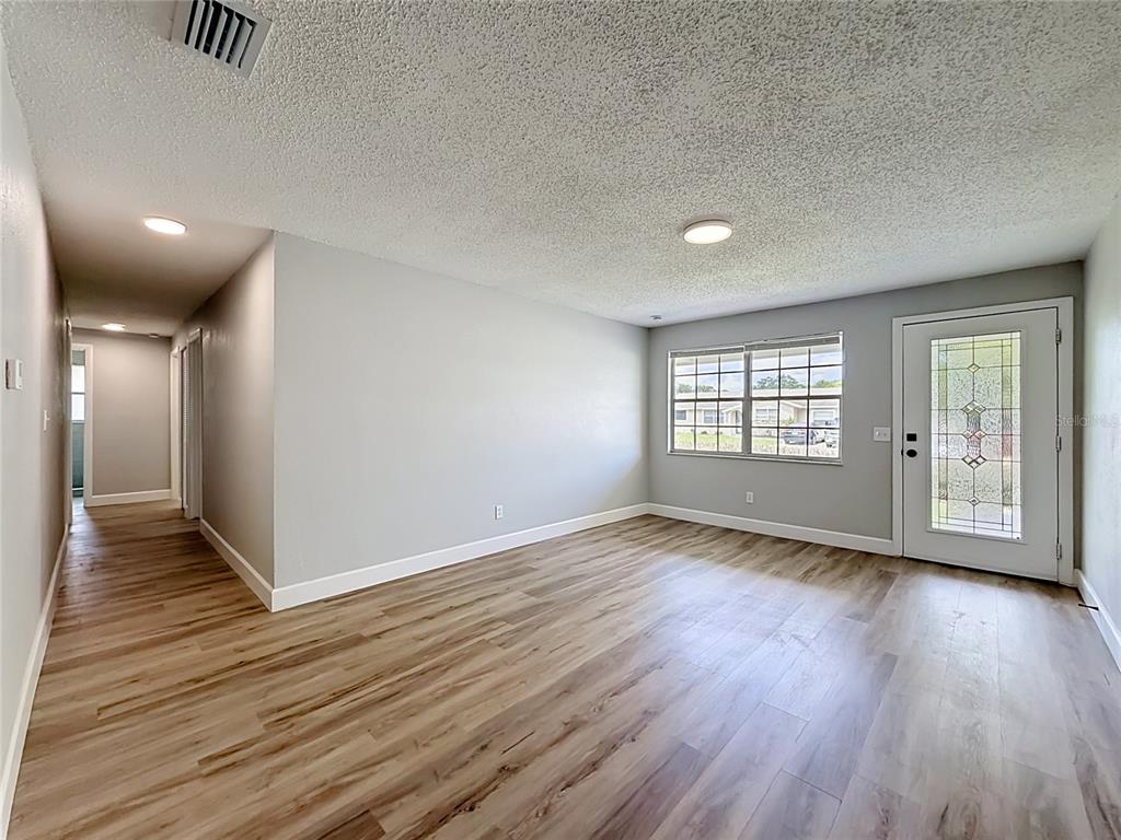 A living room with light gray walls, wood-look flooring, a textured ceiling, and a glass-paneled door — 115 DREW AVENUE, SANFORD, FL