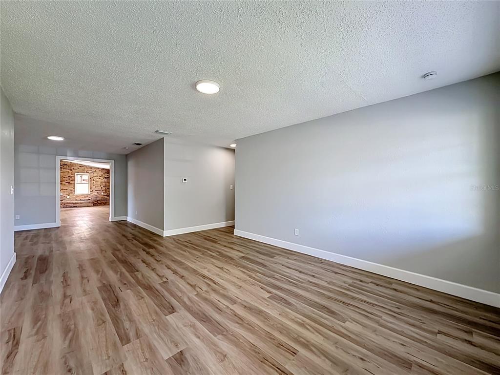 An empty room with light wood-look flooring and gray walls leads to a brick-walled space — 115 DREW AVENUE, SANFORD, FL