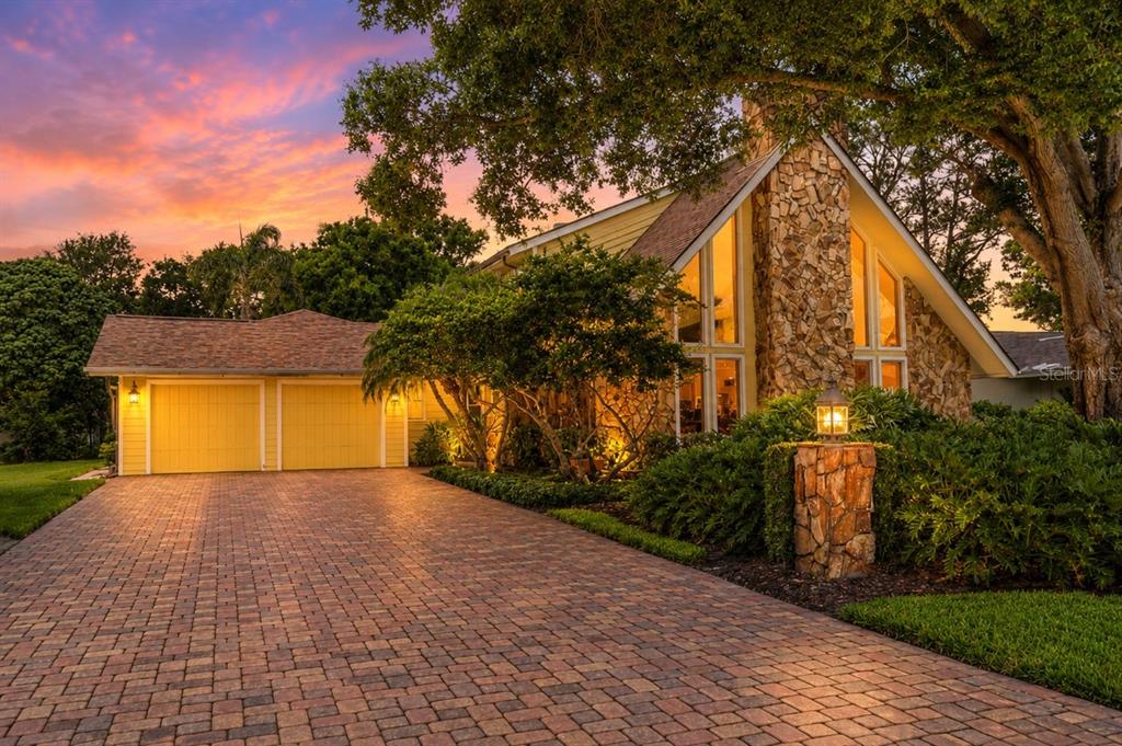 A house with a stone chimney, yellow garage doors, and a brick paver driveway at sunset — 1944 LEVINE LANE, CLEARWATER, FL
