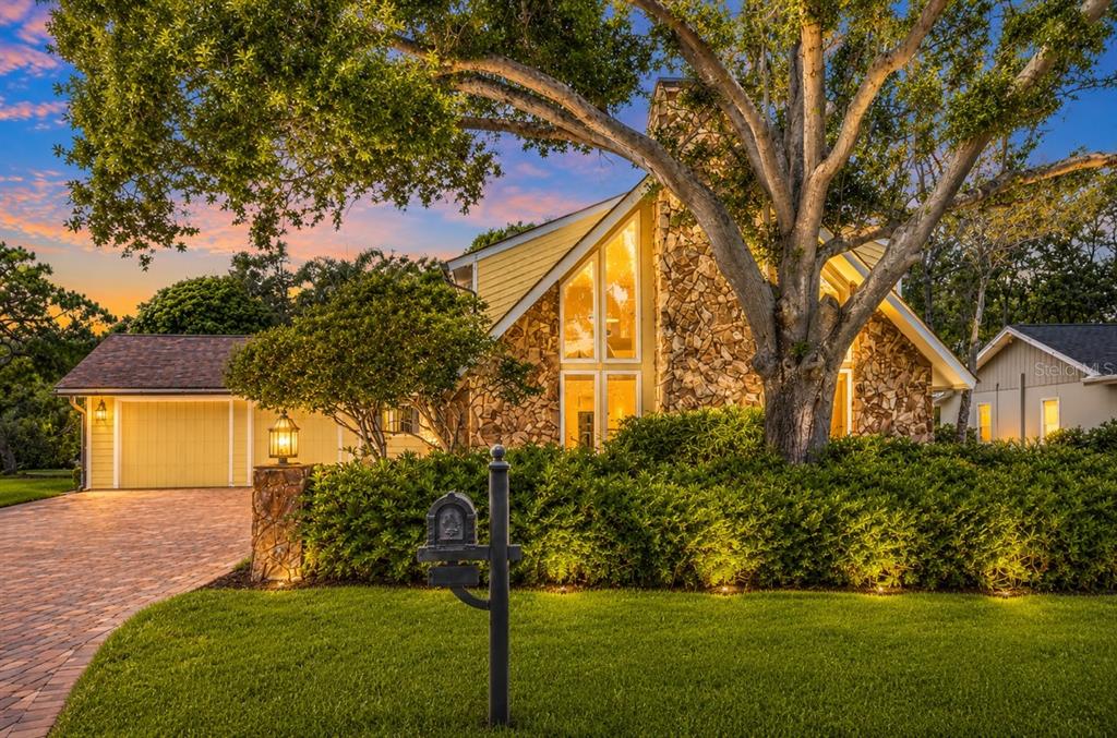 A yellow house with a stone chimney and large windows sits behind a manicured hedge — 1944 LEVINE LANE, CLEARWATER, FL