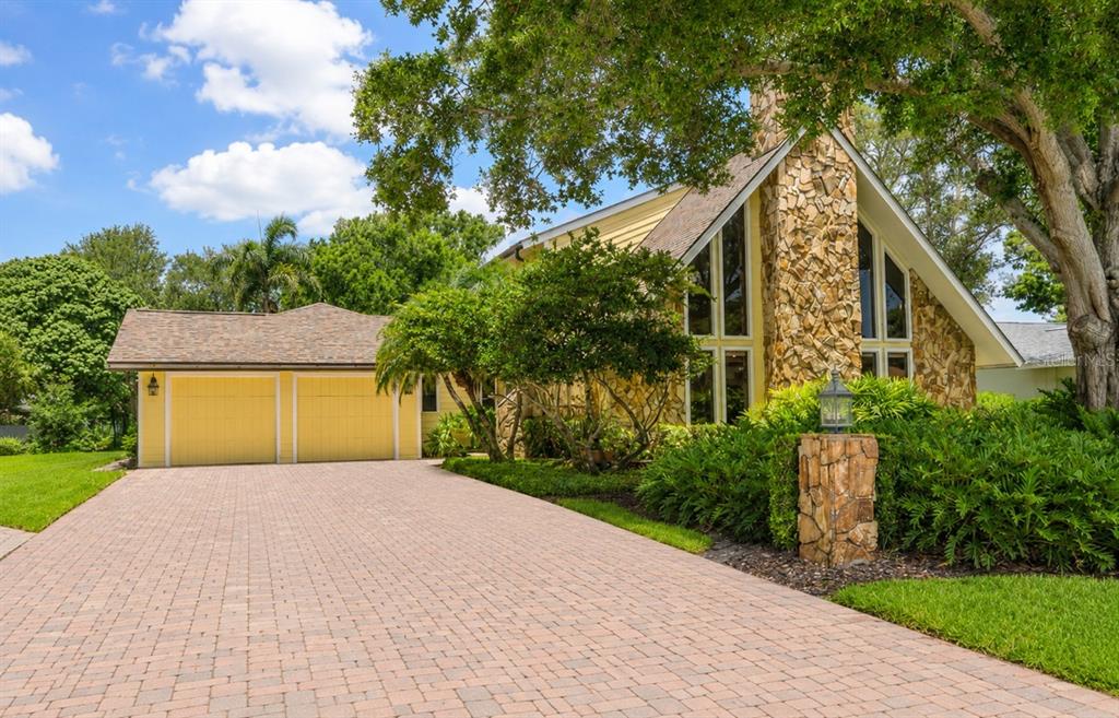 A yellow house with a stone chimney and a brick paver driveway under a large tree — 1944 LEVINE LANE, CLEARWATER, FL