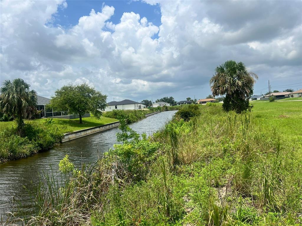 A narrow canal flows between a grassy bank and a residential property with palm trees — 225 NE 31ST STREET, CAPE CORAL, FL