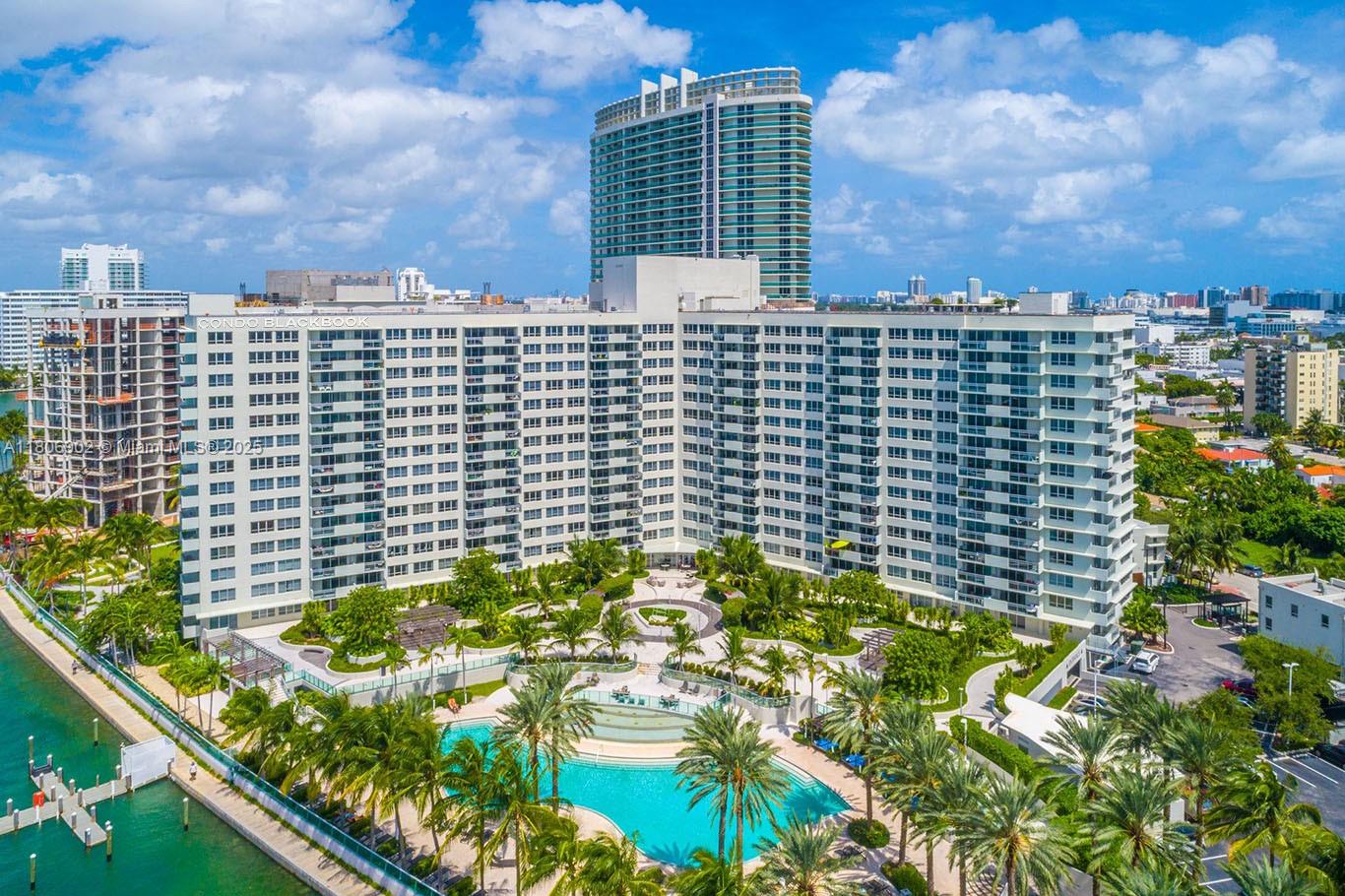 An aerial view of a large white apartment building with a pool and palm trees — 1500 Bay Rd # 1532S, Miami Beach FL 33139, MIAMI BEACH, FL