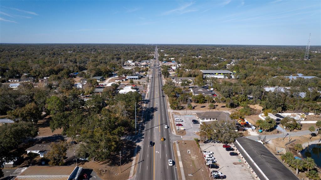 An aerial view shows a multi-lane road stretching through a wooded area with scattered buildings — S VOLUSIA AVENUE, ORANGE CITY, FL