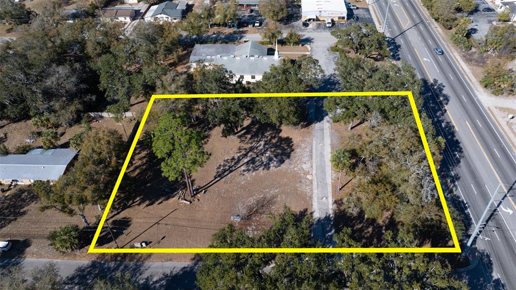 An aerial view shows a vacant, tree-covered rectangular lot outlined in yellow next to a road — S VOLUSIA AVENUE, ORANGE CITY, FL