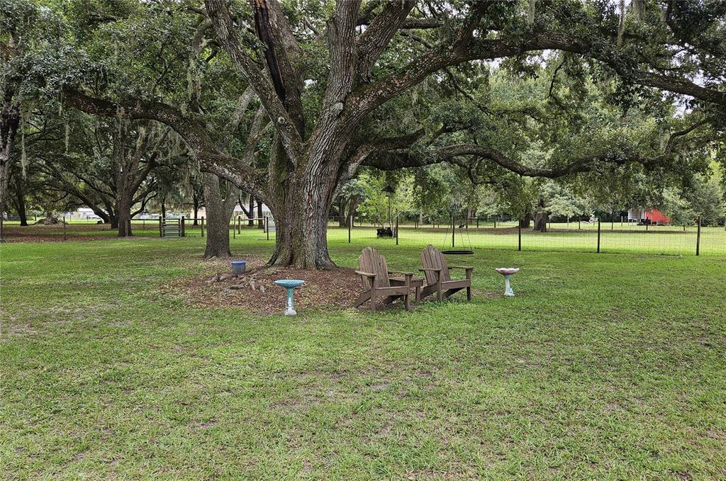 A white detached garage stands next to a wooden carport on a grassy, tree-shaded lot — 5136 SHEPARD LANE, POLK CITY, FL