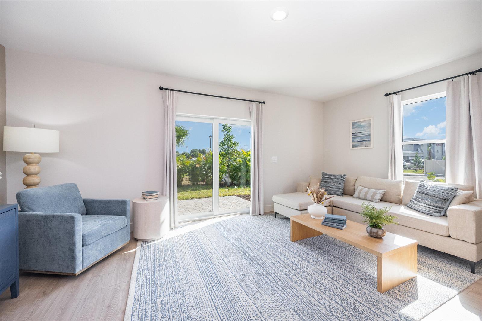 A living room features a beige sectional, blue armchair, area rug, and sliding glass doors — 8136 Cobblestone Drive, Fort Pierce FL 34945, FORT PIERCE, FL
