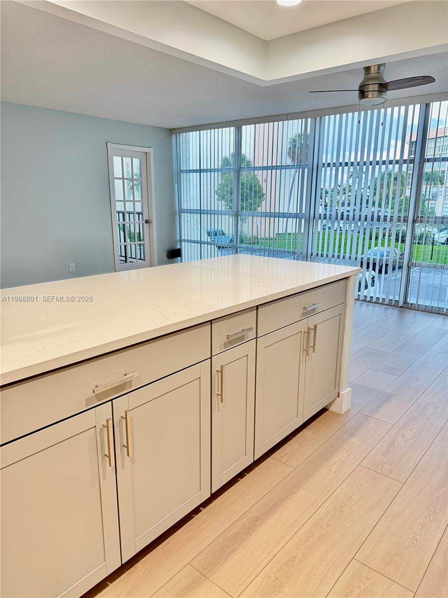 A kitchen island with light-colored cabinets and a white countertop sits on wood-look flooring — 601 Three Islands Blvd # 217, Hallandale Beach FL 33009, HALLANDALE BEACH, FL