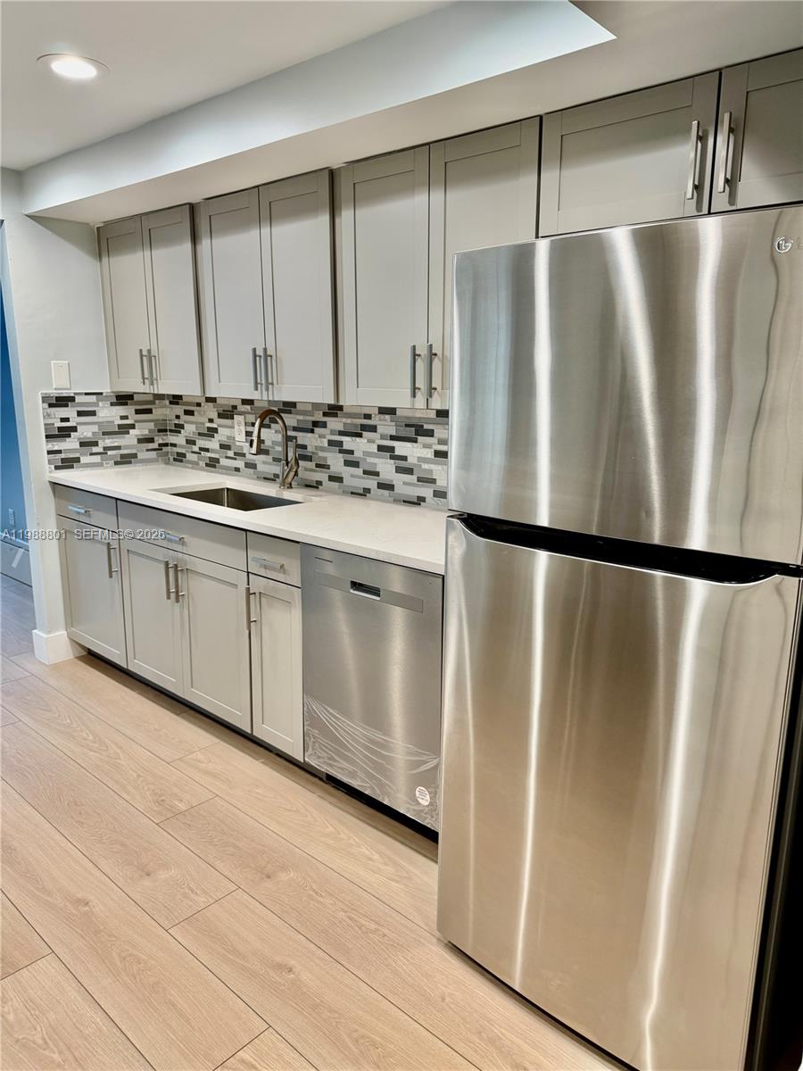A kitchen features light gray cabinets, stainless steel appliances, and a mosaic tile backsplash — 601 Three Islands Blvd # 217, Hallandale Beach FL 33009, HALLANDALE BEACH, FL