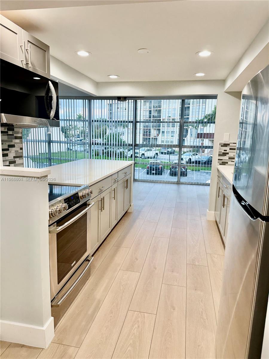 A modern kitchen features light-colored cabinetry, stainless steel appliances, and large floor-to-ceiling windows — 601 Three Islands Blvd # 217, Hallandale Beach FL 33009, HALLANDALE BEACH, FL
