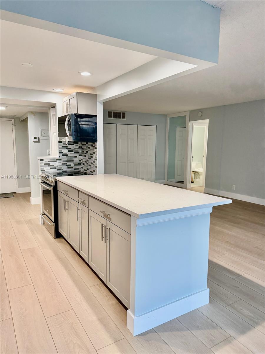 A kitchen island with light gray cabinets and a white countertop sits in an open-concept room — 601 Three Islands Blvd # 217, Hallandale Beach FL 33009, HALLANDALE BEACH, FL