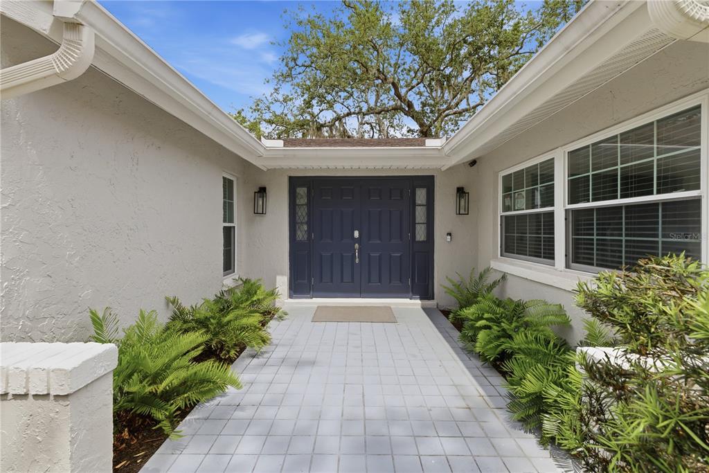 A paved walkway leads to a dark blue double front door between two stucco walls — 1389 PONCE DE LEON BOULEVARD, WINTER SPRINGS, FL
