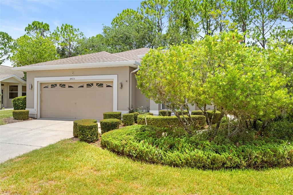 A beige house with a two-car garage and manicured landscaping sits under a blue sky — 14425 STERLING RUN, SPRING HILL, FL