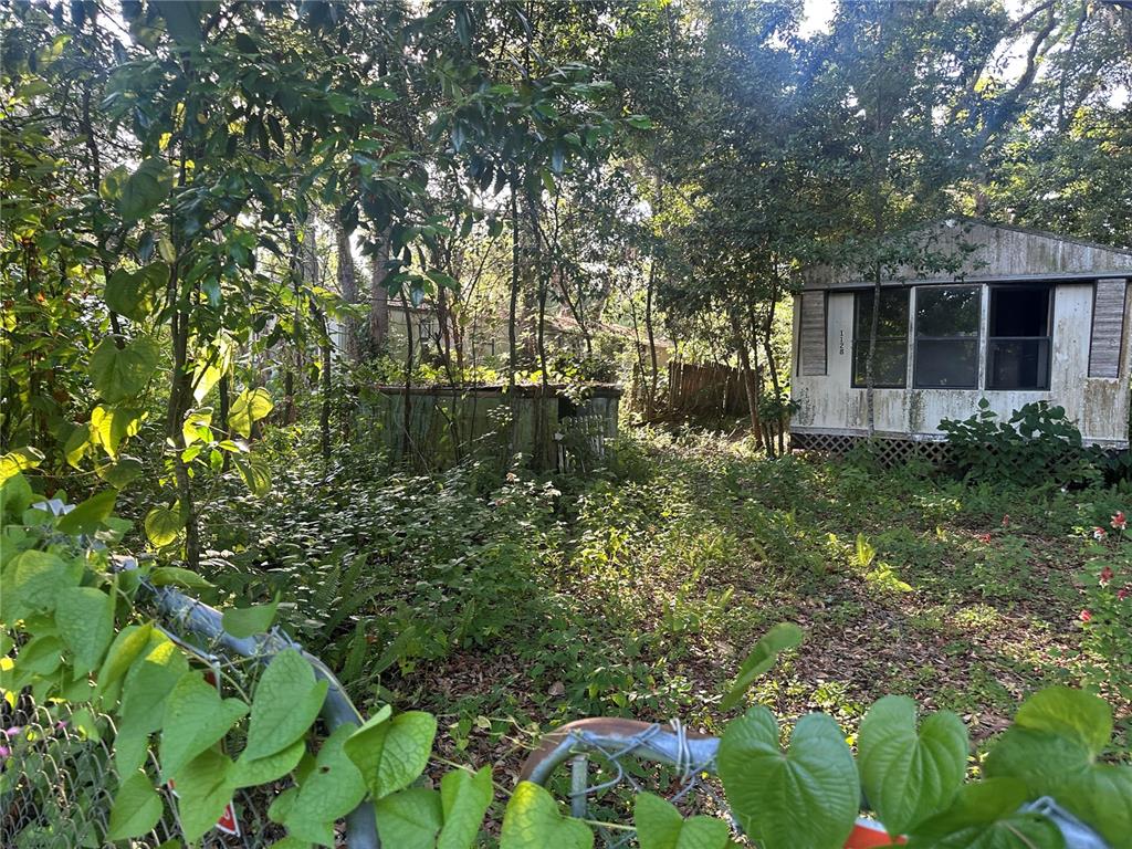 An overgrown lot features a weathered mobile home and a small, dilapidated shed — 1128 N JACKSON AVENUE S, SPRING HILL, FL