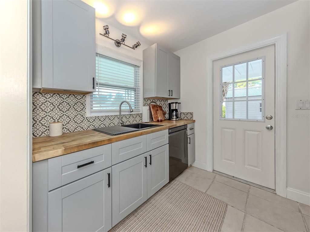 A kitchen features light gray cabinets, a wood countertop, patterned backsplash, and a glass-paneled door — 929 CYPRESS AVENUE, VENICE, FL
