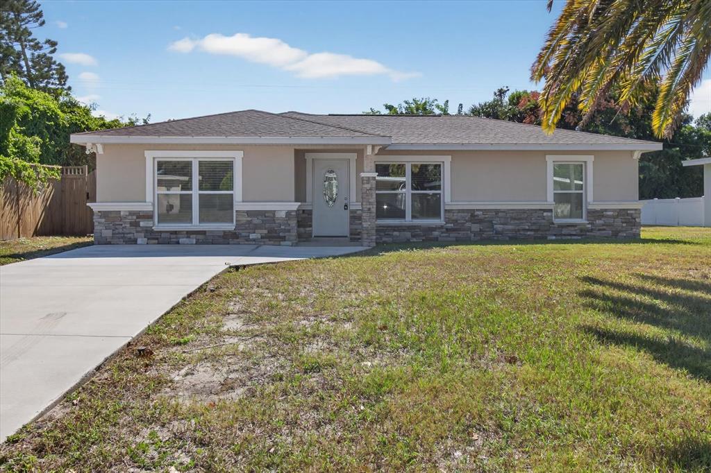 A single-story house with a beige stucco exterior, stone veneer accents, and a concrete driveway — 5352 TANGERINE DRIVE, NEW PORT RICHEY, FL