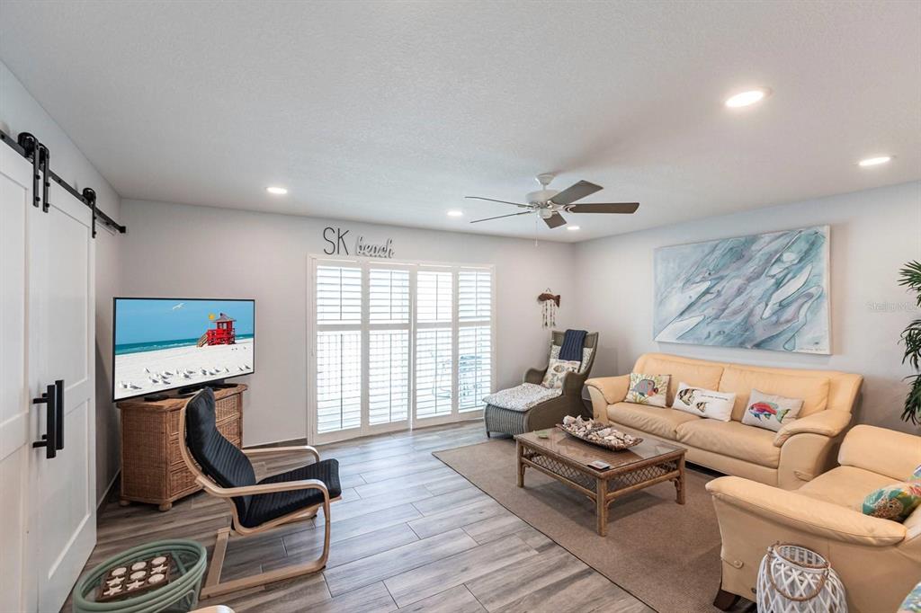 A living room features light wood-look tile floors, a beige sofa, and a television stand — 6154 MIDNIGHT PASS ROAD UNIT 202, SARASOTA, FL
