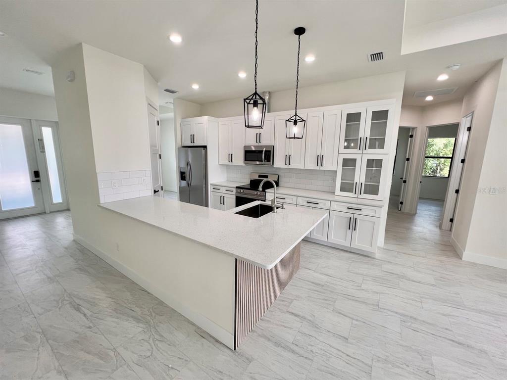 A modern kitchen features white cabinetry, a quartz-topped island, and light-colored tile flooring — 9245 BOCA GRANDE AVENUE, ENGLEWOOD, FL