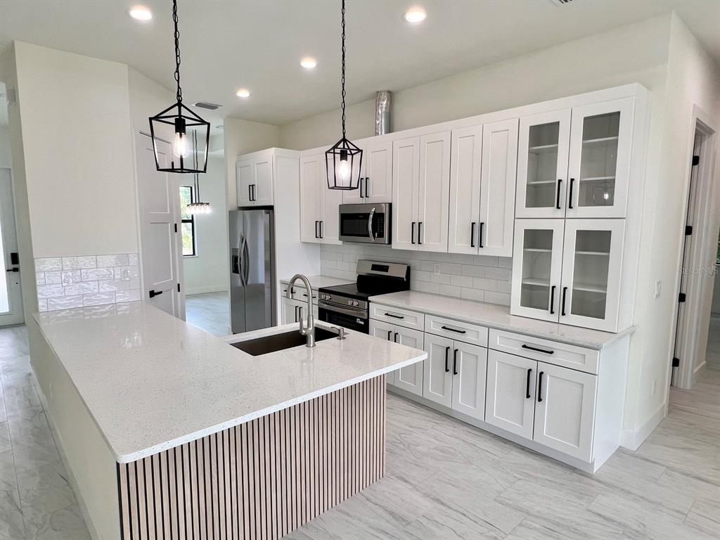 A modern kitchen features white cabinetry, quartz countertops, a slatted island, and stainless steel appliances — 9245 BOCA GRANDE AVENUE, ENGLEWOOD, FL
