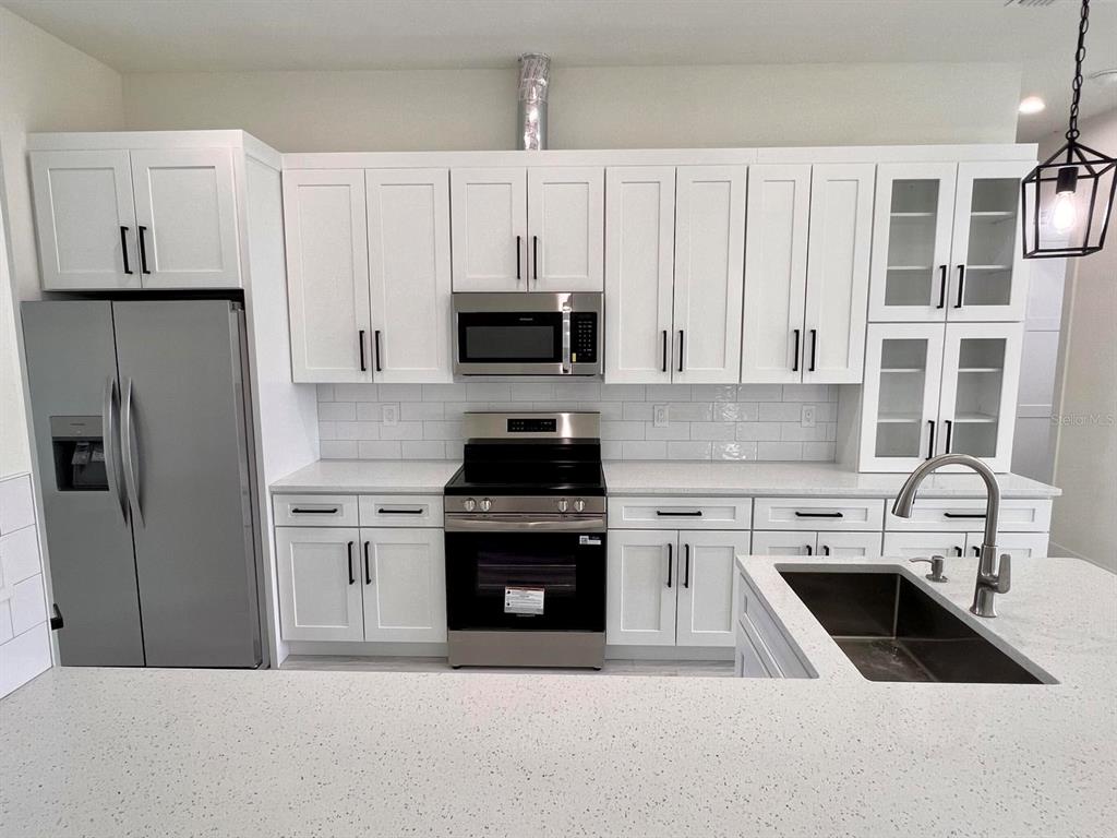 A kitchen features white cabinets, stainless steel appliances, a subway tile backsplash, and quartz countertops — 9245 BOCA GRANDE AVENUE, ENGLEWOOD, FL