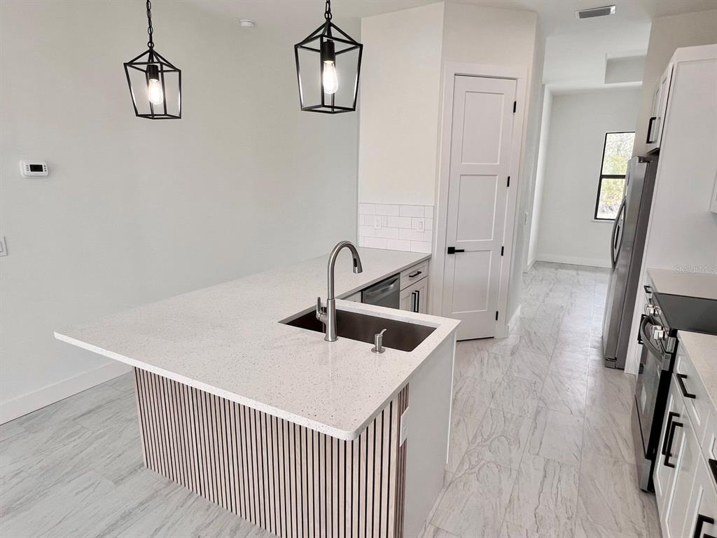 A modern kitchen features a white quartz island with a slatted base and pendant lighting — 9245 BOCA GRANDE AVENUE, ENGLEWOOD, FL