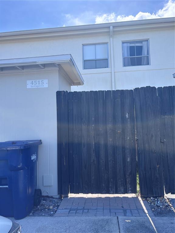 A blue trash bin sits next to a wooden privacy fence in front of a building — 4515 LA CAPRI COURT, TAMPA, FL