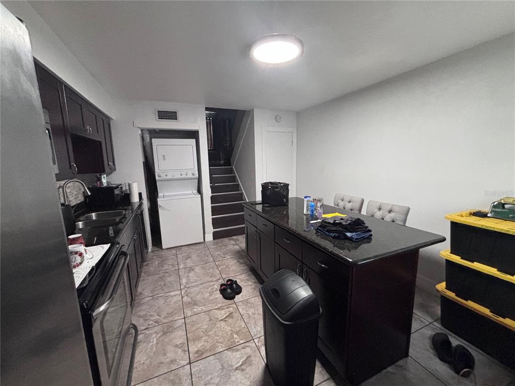 A kitchen features dark cabinetry, a granite-topped island, tile flooring, and a stacked laundry unit — 4515 LA CAPRI COURT, TAMPA, FL