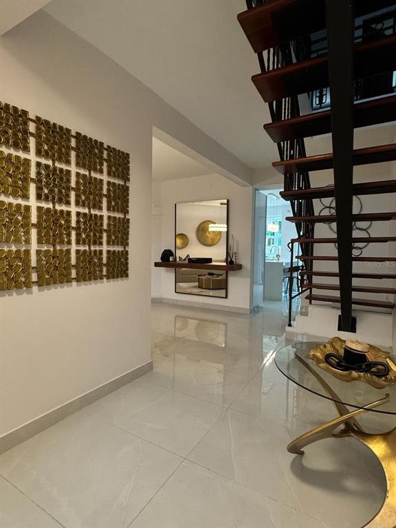 A modern entryway features a floating staircase, large gold wall art, and polished tile flooring — B7 BRIGHTON COUNTRY CLUB, DORADO, PR