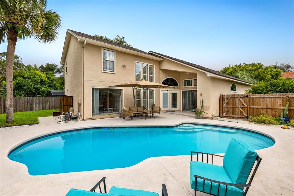 A two-story house with a beige stucco exterior overlooks a backyard swimming pool and patio — 933 BEARDED OAKS TERRACE, LONGWOOD, FL