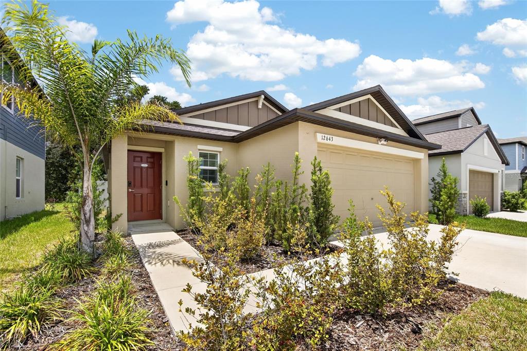 A single-story suburban house features a tan stucco exterior, a red front door, and a garage — 12643 MAPLE BONSAI DRIVE, RIVERVIEW, FL