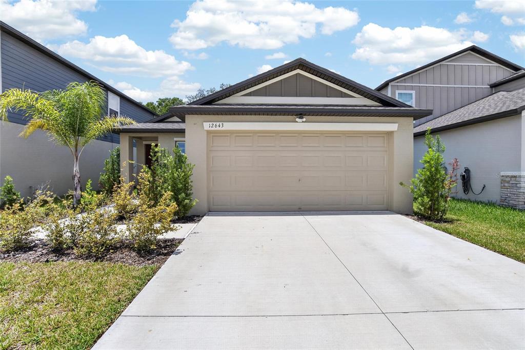 A single-story house features a beige stucco exterior, a two-car garage, and a concrete driveway — 12643 MAPLE BONSAI DRIVE, RIVERVIEW, FL