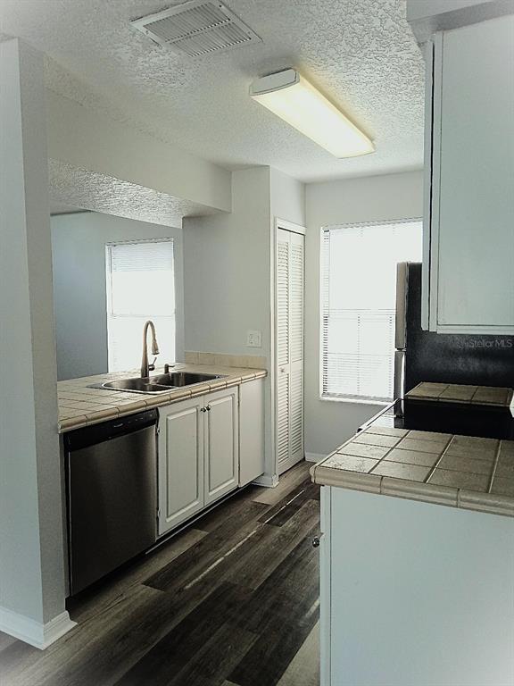 A kitchen features white cabinets, tiled countertops, stainless steel appliances, and wood-look flooring — 2931 RIO GRANDE TRL UNIT D, KISSIMMEE, FL