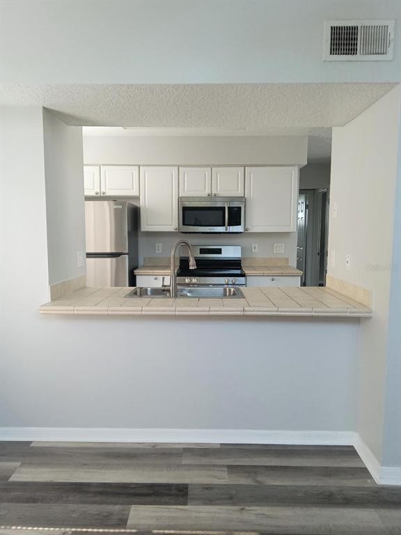 A kitchen with white cabinets, stainless steel appliances, and a tiled breakfast bar counter — 2931 RIO GRANDE TRL UNIT D, KISSIMMEE, FL