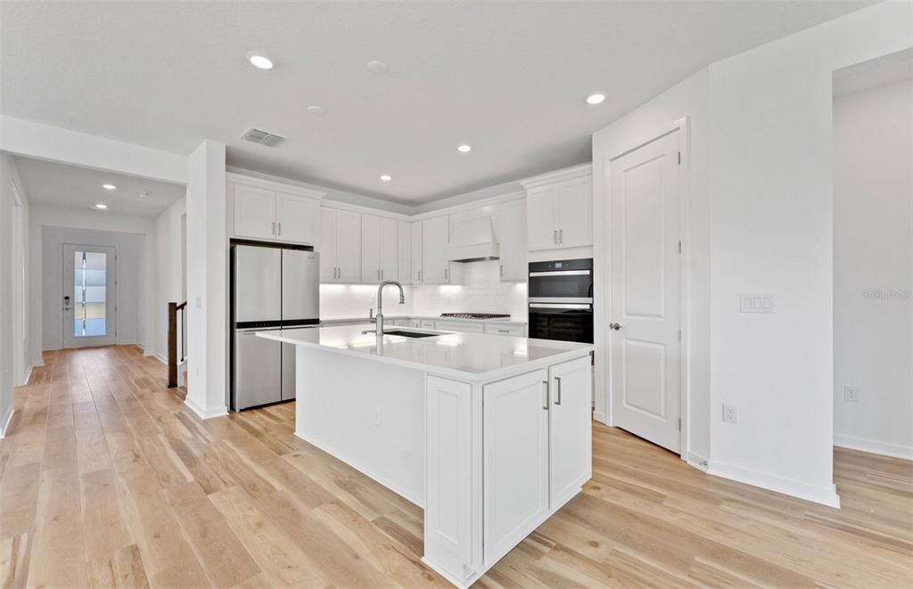 A modern kitchen features white cabinetry, a central island, stainless steel appliances, and wood flooring — 13816 SUNLIGHT MEADOW DRIVE, RIVERVIEW, FL