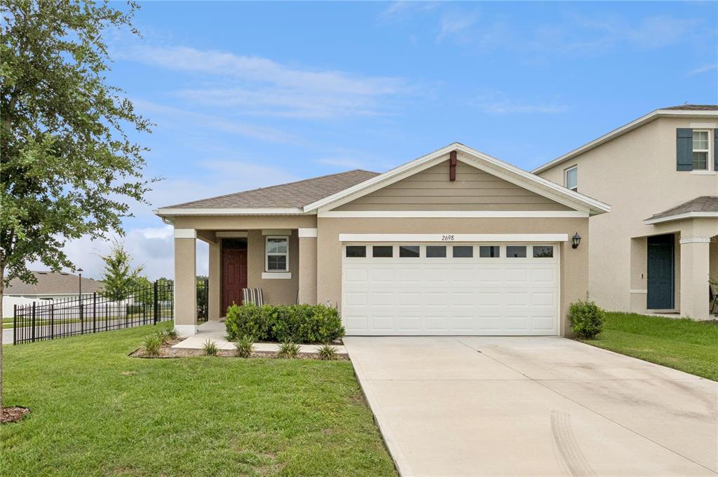 A single-story house with a beige exterior, a two-car garage, and a covered front porch — 2698 ROWAN STREET, TAVARES, FL
