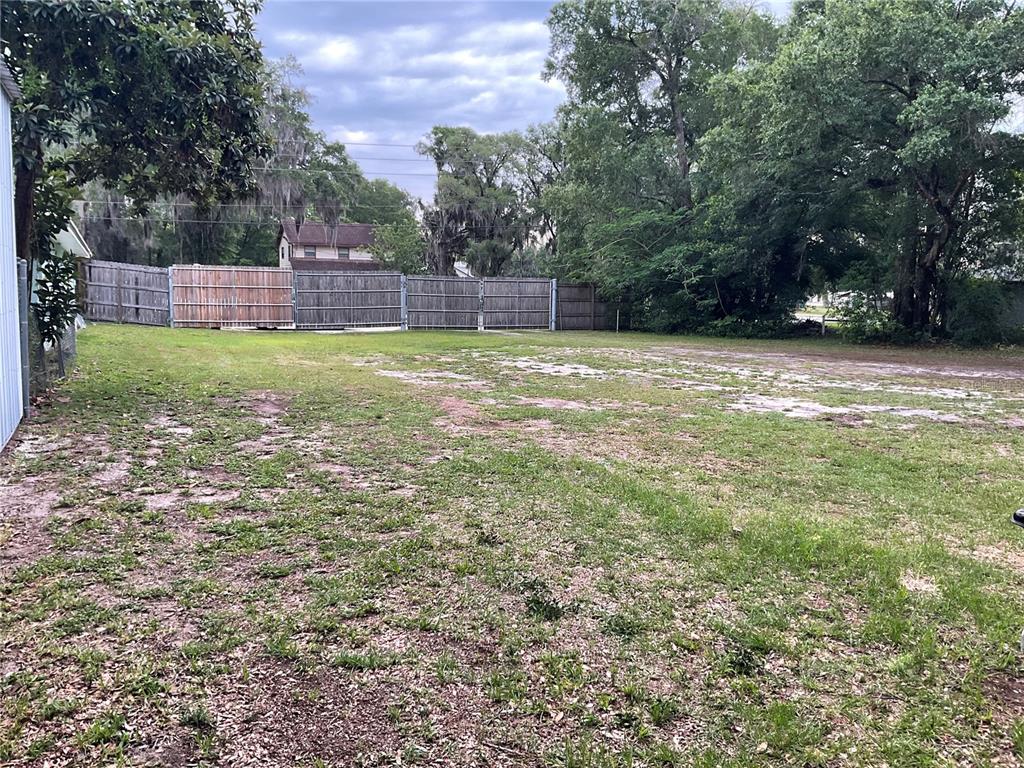 A grassy, vacant lot features a wooden privacy fence and mature trees in the background — 360 S LAKEVIEW DRIVE, LAKE HELEN, FL