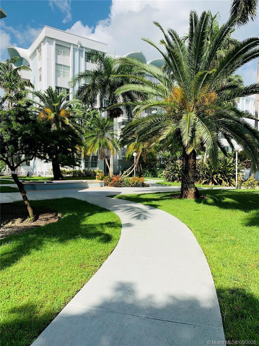 A paved walkway leads through a landscaped courtyard toward a multi-story white apartment building — 488 NW 165th St Rd # 610, Miami FL 33169, MIAMI, FL