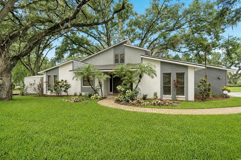A single-story house with white stucco and gray siding sits behind a curved brick walkway — 1904 CAPRI ROAD, VALRICO, FL