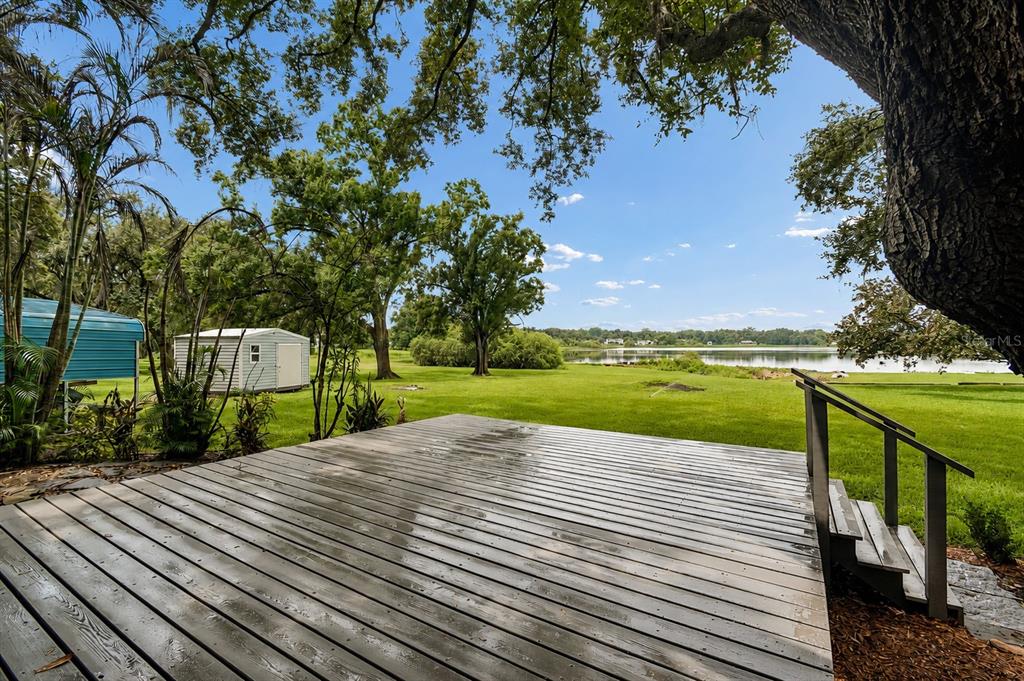 A wooden deck overlooks a grassy backyard with a storage shed and a lake beyond — 1904 CAPRI ROAD, VALRICO, FL
