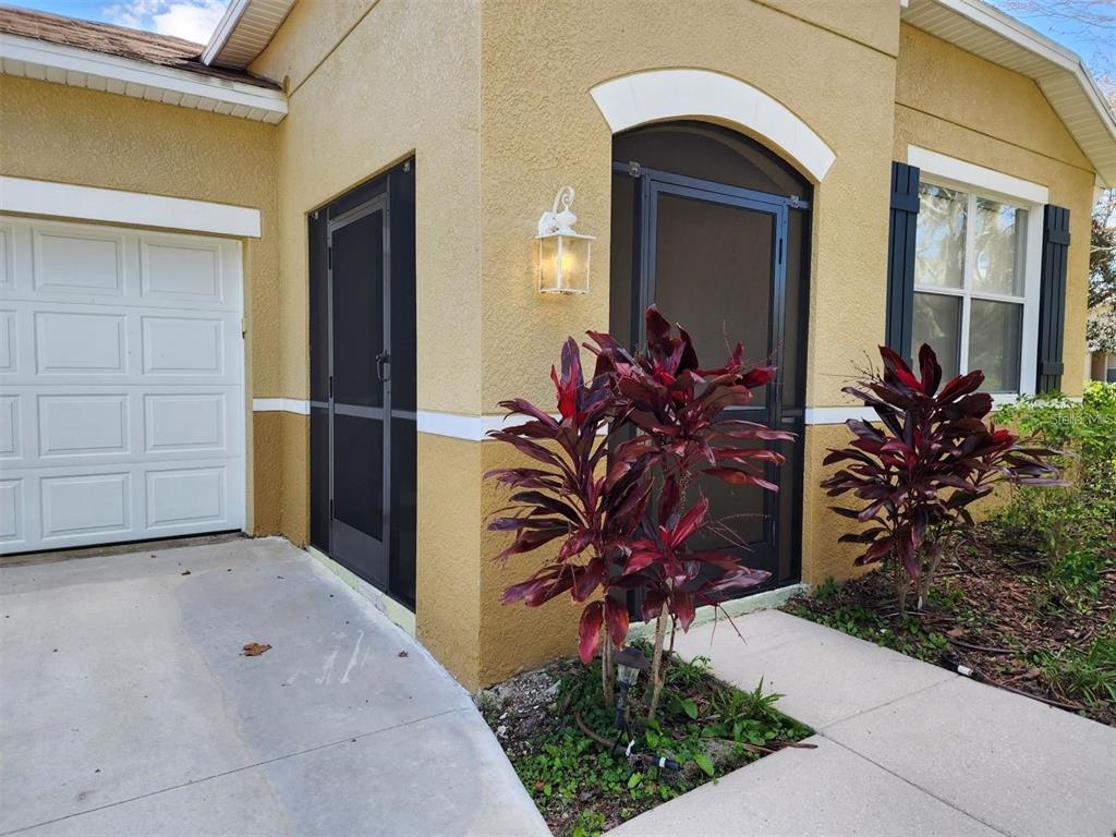 The exterior of a yellow house features two screen doors, a garage, and red plants — 107 SLIPPER KEY ROAD, APOLLO BEACH, FL