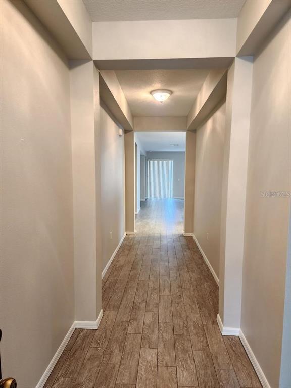 A hallway with light-colored walls and wood-look tile flooring leads toward a bright living area — 107 SLIPPER KEY ROAD, APOLLO BEACH, FL