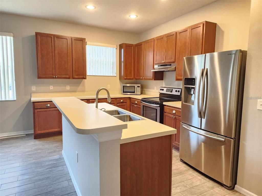 A kitchen features wood cabinets, stainless steel appliances, a center island, and light-colored countertops — 107 SLIPPER KEY ROAD, APOLLO BEACH, FL