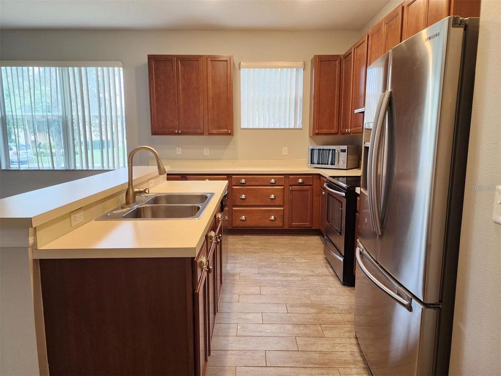 A kitchen features wood cabinets, stainless steel appliances, a double sink, and light-colored countertops — 107 SLIPPER KEY ROAD, APOLLO BEACH, FL