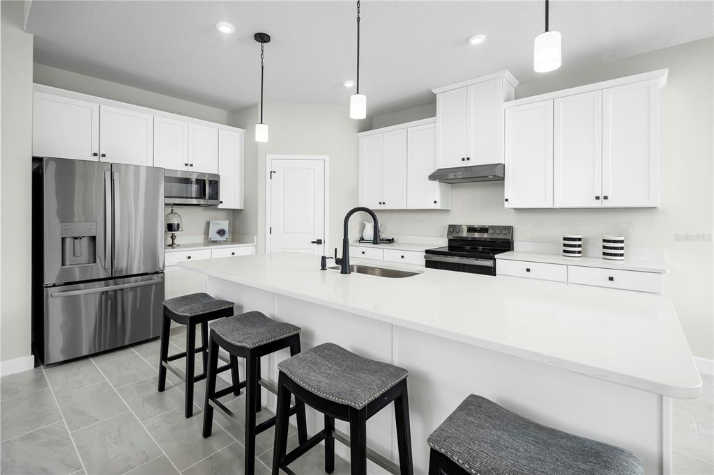 A modern kitchen features white cabinetry, stainless steel appliances, and a large central island — 3255 TIGER PALM WAY, NEW SMYRNA BEACH, FL
