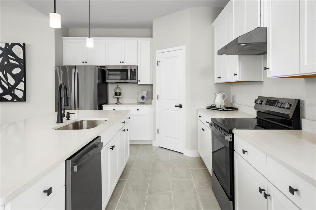 A modern kitchen features white cabinets, stainless steel appliances, a center island, and tile flooring — 3255 TIGER PALM WAY, NEW SMYRNA BEACH, FL