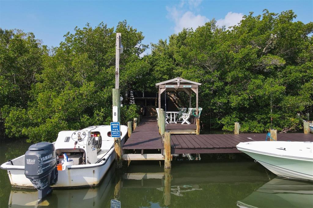 A wooden dock with a covered seating area sits between two boats near dense trees — 8144 LITTLE GASPARILLA ISLAND, PLACIDA, FL